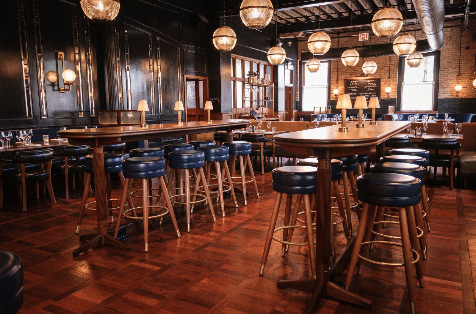 Spacious restaurant interior with wooden tables, blue cushioned stools, parquet flooring, and globe pendant lights