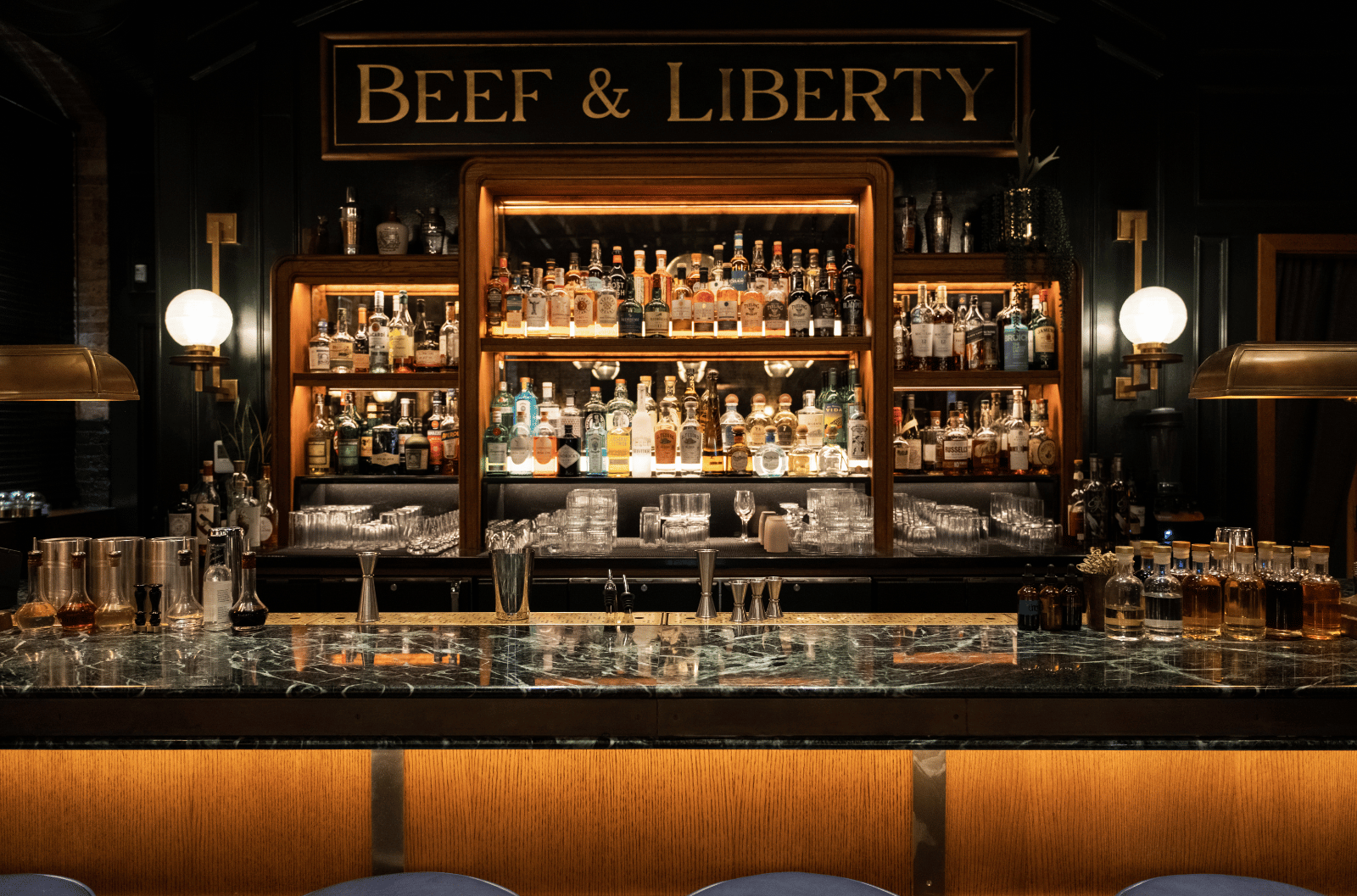 Close-up view of the illuminated "Beef & Liberty" bar with various spirits, glassware, and modern decor.