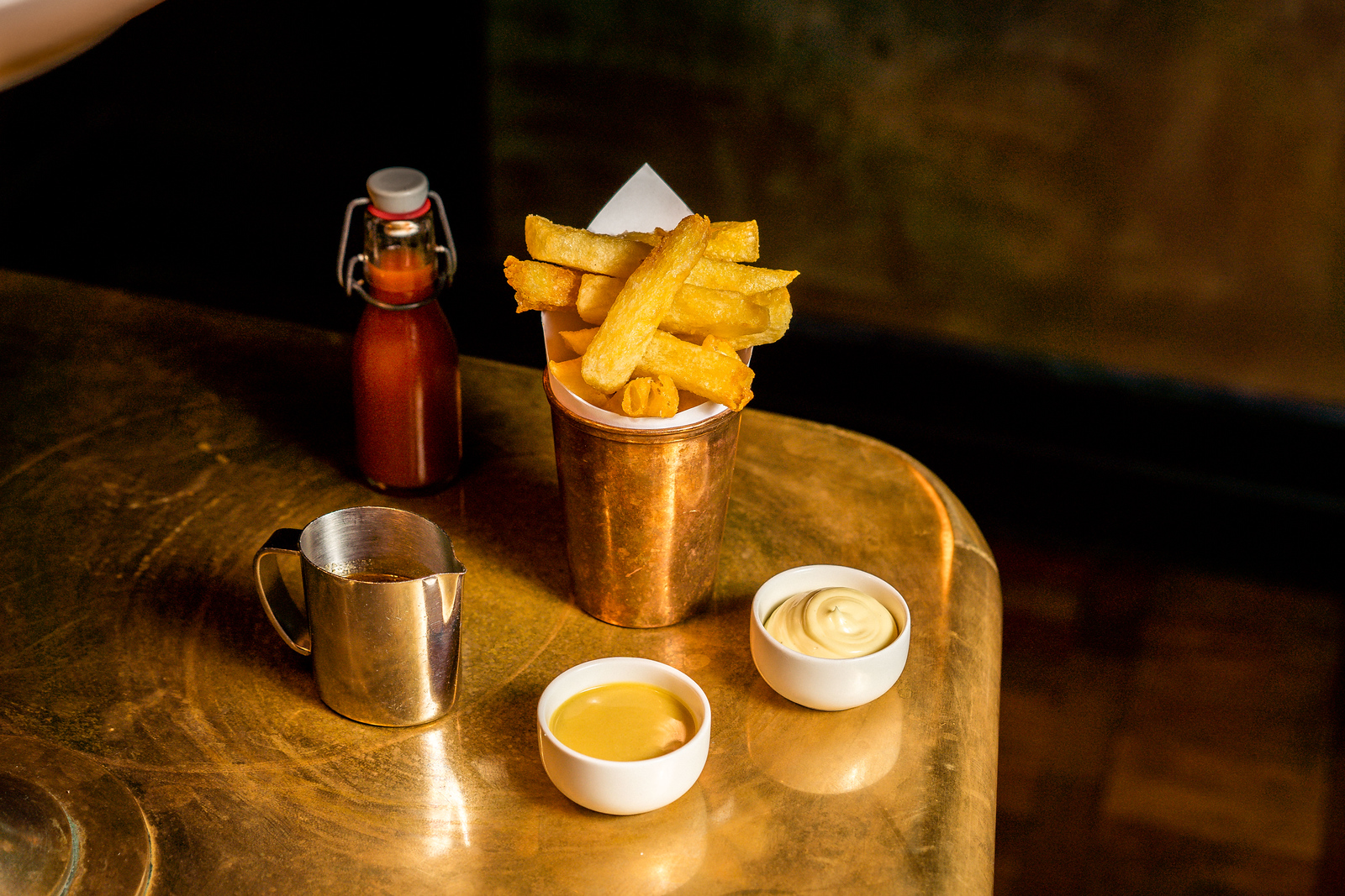 A pot of beef-dripping chips with homemade condiments on a golden table
