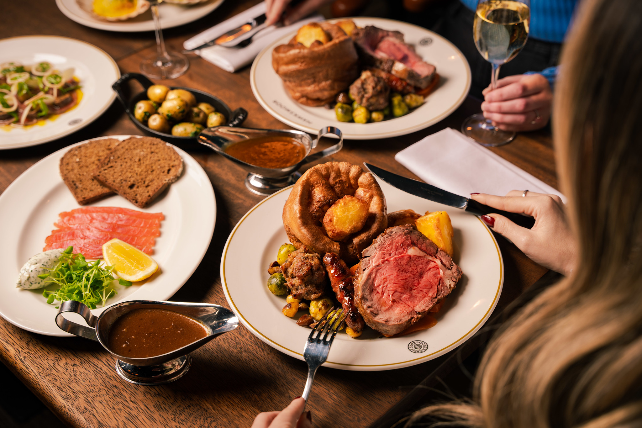 Sunday roast at Hawksmoor: roast beef with a Yorkshire pudding, roast potatoes and greens, with gravy and side dishes on a shared table