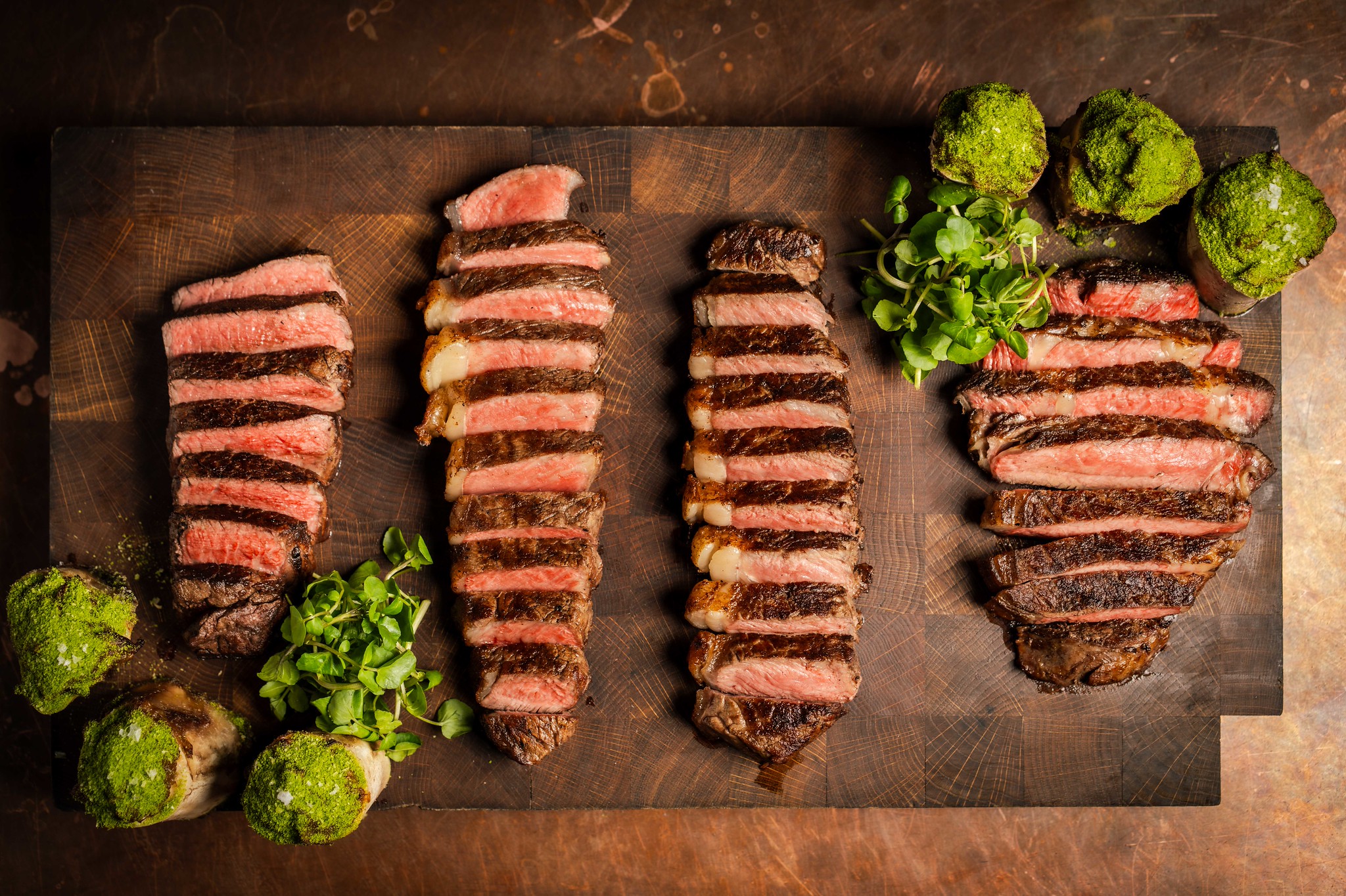 Hawksmoor US steak flight, four sliced cuts on a board: grass-fed Black Angus filet, Wagyu strip, Akaushi strip and Black Angus rib-eye