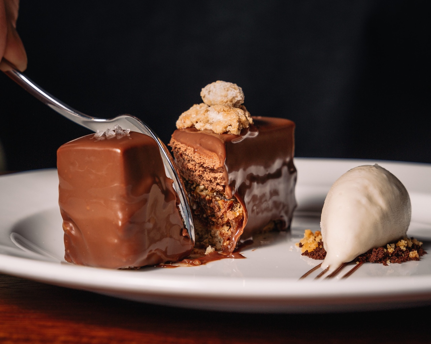 A decadent Chocolate mille-feuille on a white plate being cut in half with a folk. To the right of the Chocolate mille-feuille is a dollop of thick clotted cream.