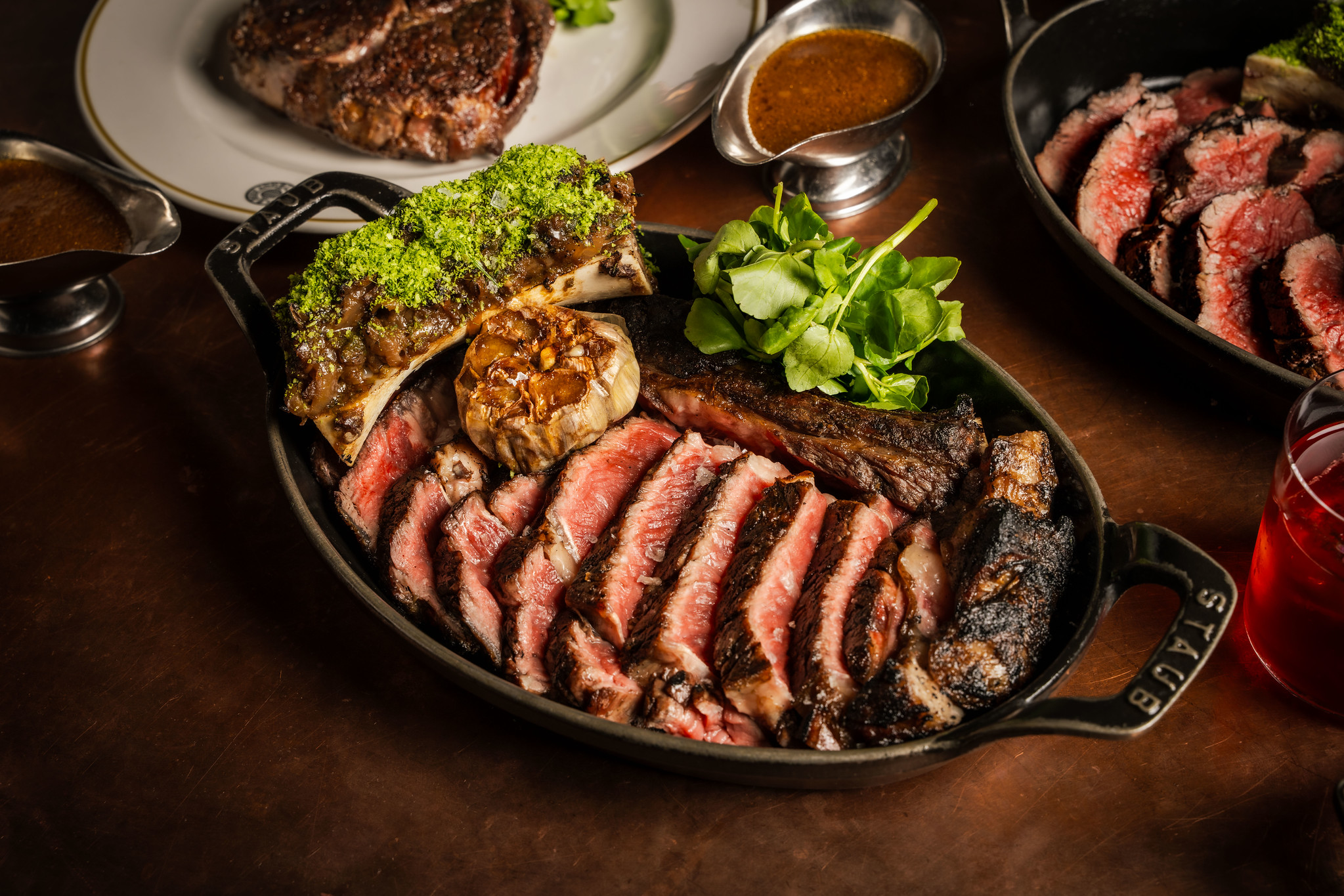 An overhead shot of a sharing steak, served in a cast iron dish, sliced up, with a side of herbed bone marrow