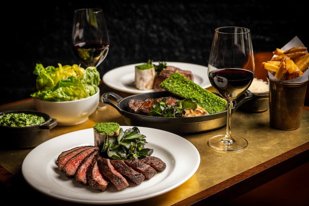 A shiny gold coloured table laden with sliced wagyu steak dishes, sides of fries and creamed cabbage and a red wine.