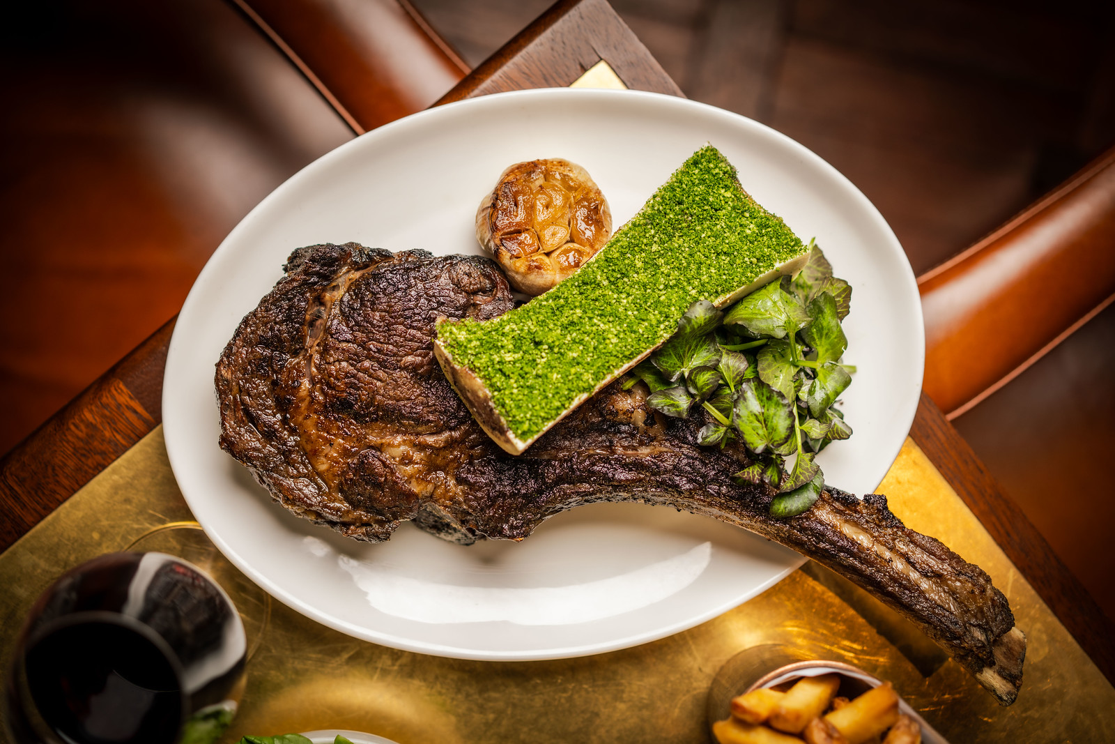A long bone rib chops on a white plate with a side of bone marow with green garlic-parsley crumb