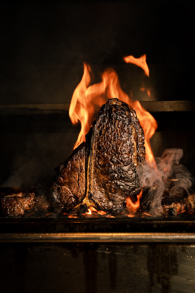A large steak on the bone pictured on the grill against flames