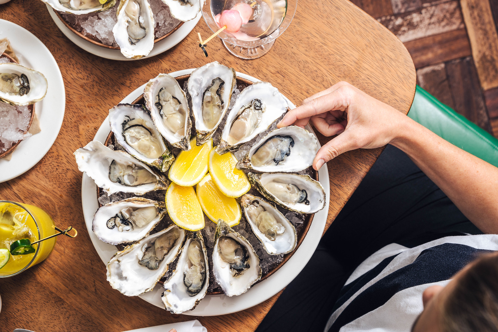 A platter of fresh oysters with a lemon garnish. A hand picking up an oyster