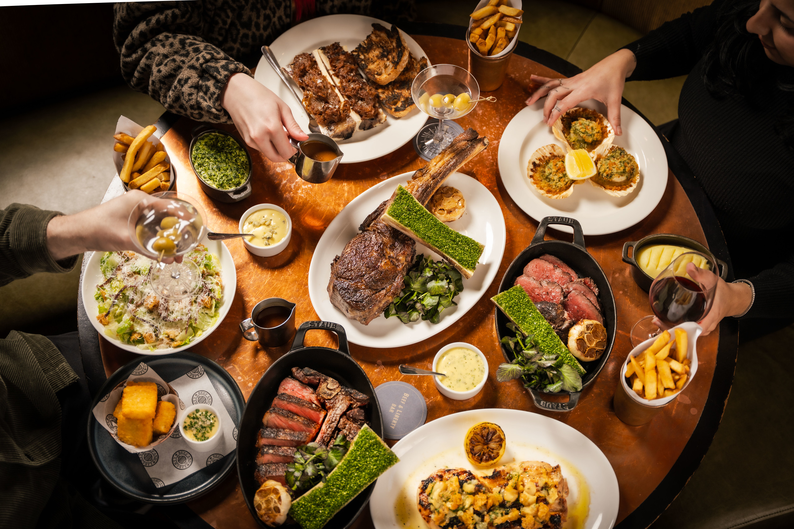 An overhead shot of the table laden with various cuts of steak nin skillets, starters and side dishes