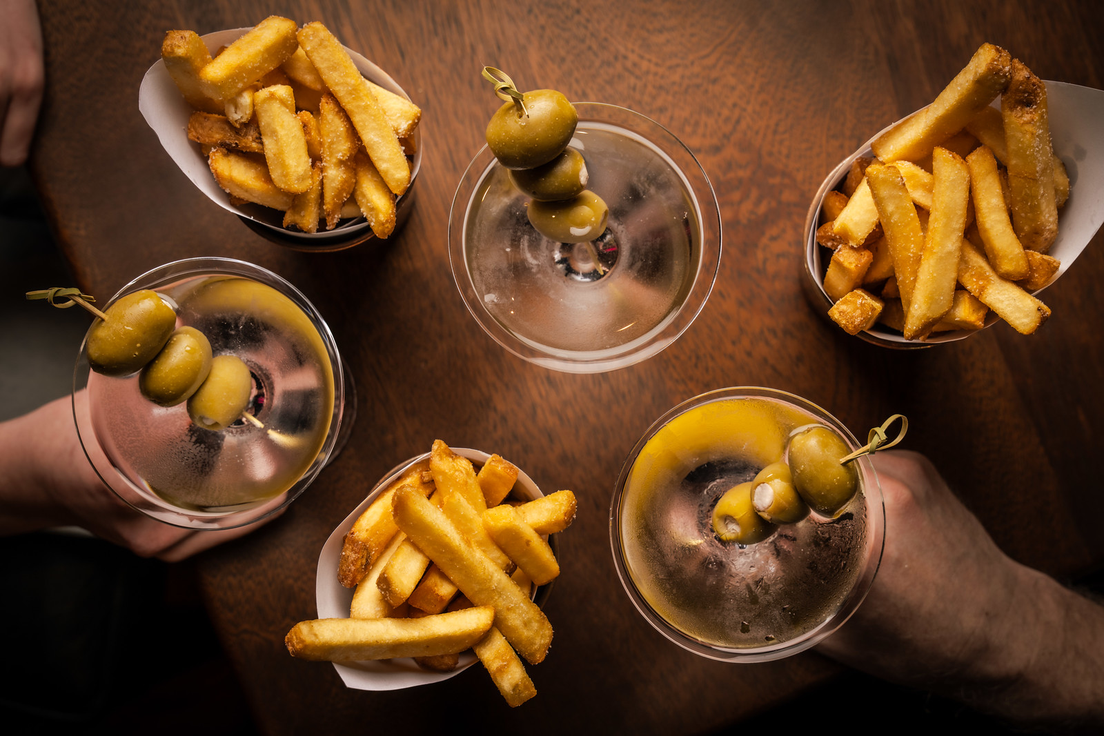 An overhead shot of a table with three martinis and three pots of beef dripping chips