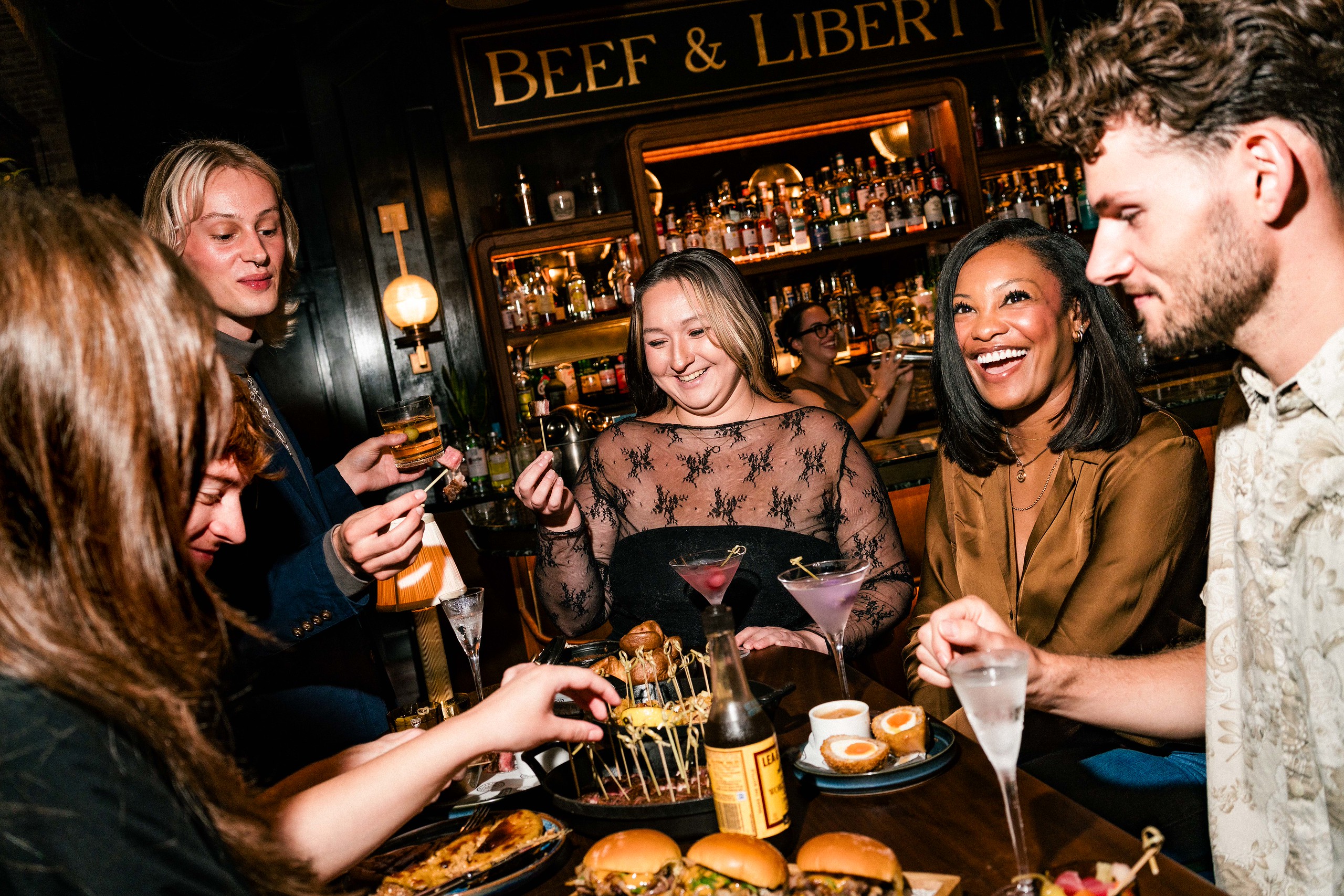 A group of friends around a table, laughing and raising glasses