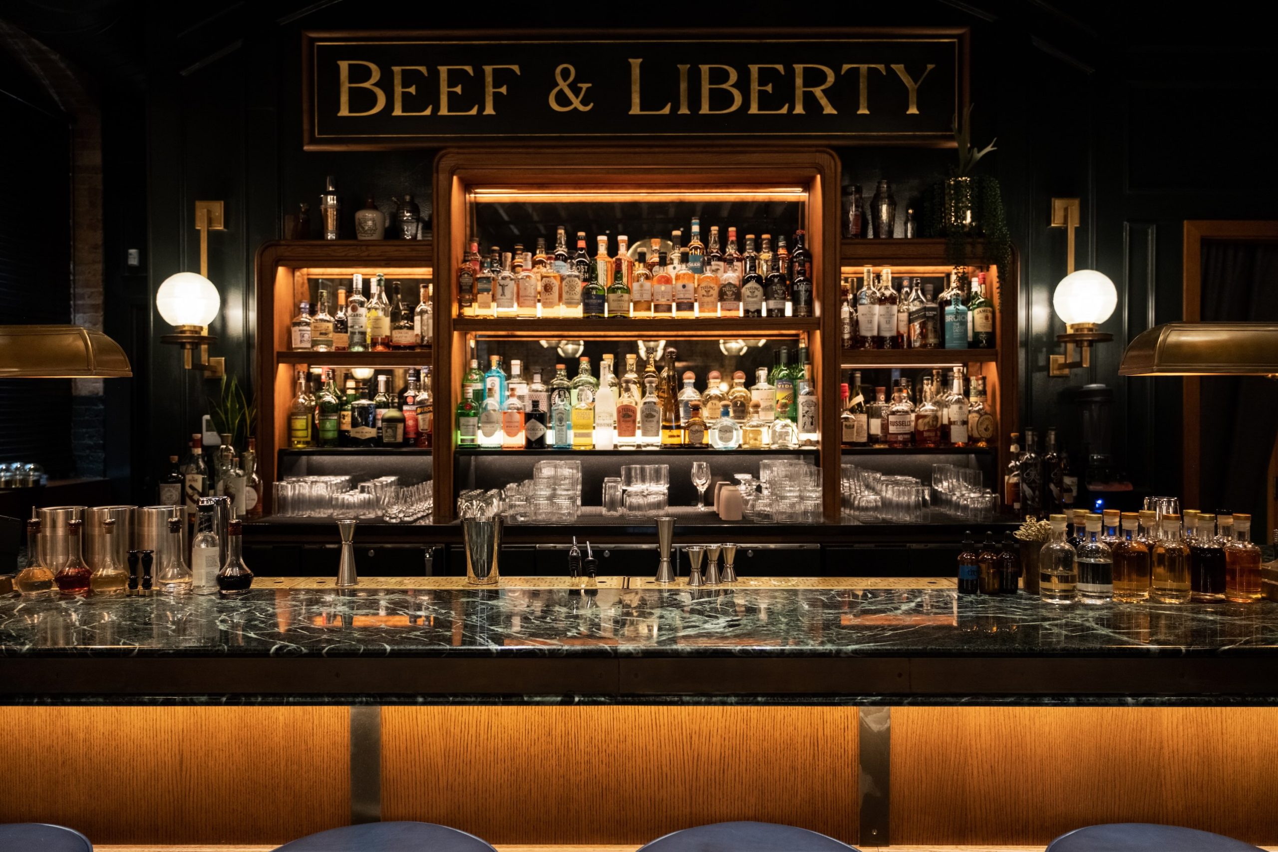 Close-up view of the illuminated "Beef & Liberty" bar with various spirits, glassware, and modern decor.