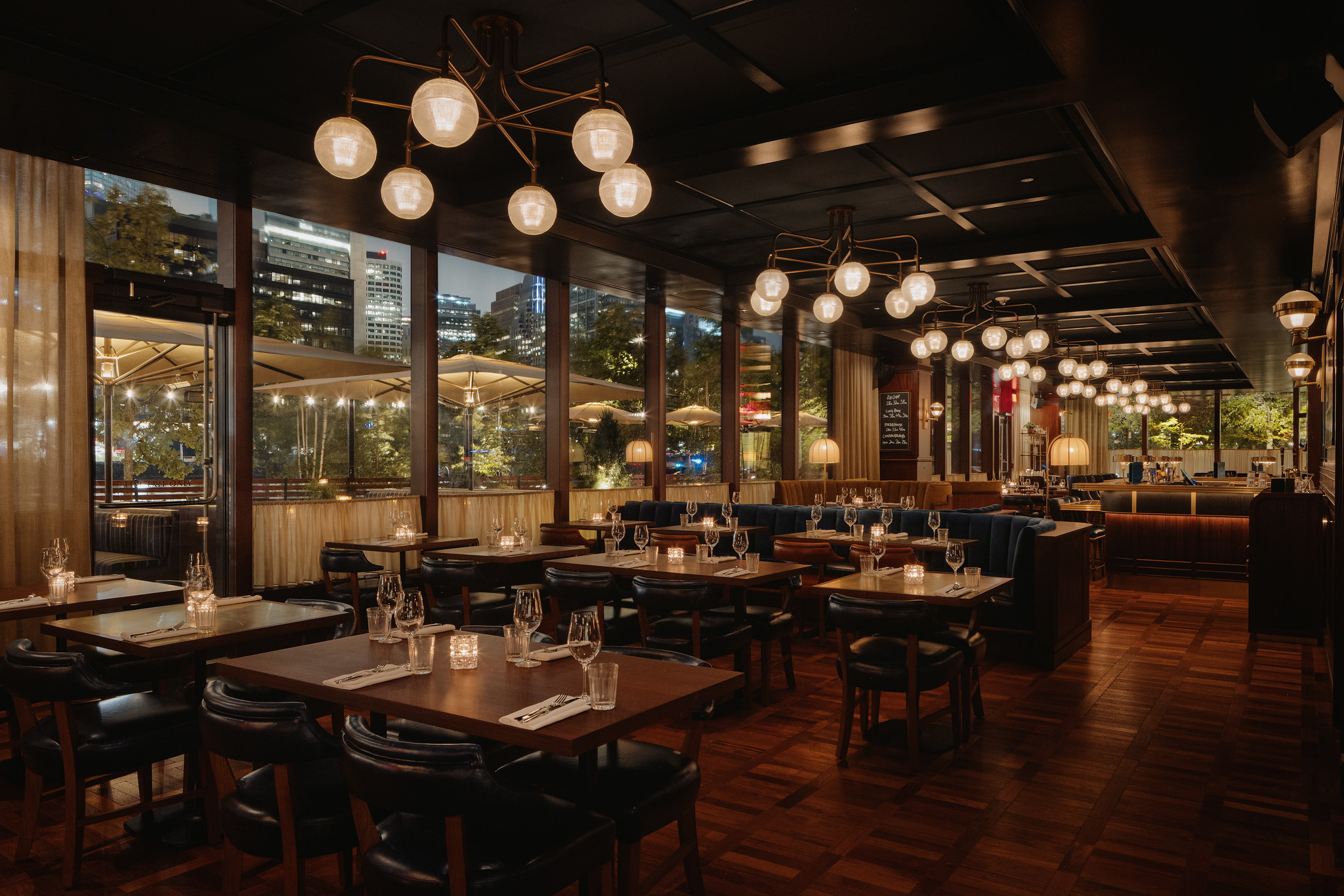 Dining room at Hawksmoor Boston, with dark wood tables, leather seating and globe pendant lights beneath tall windows.