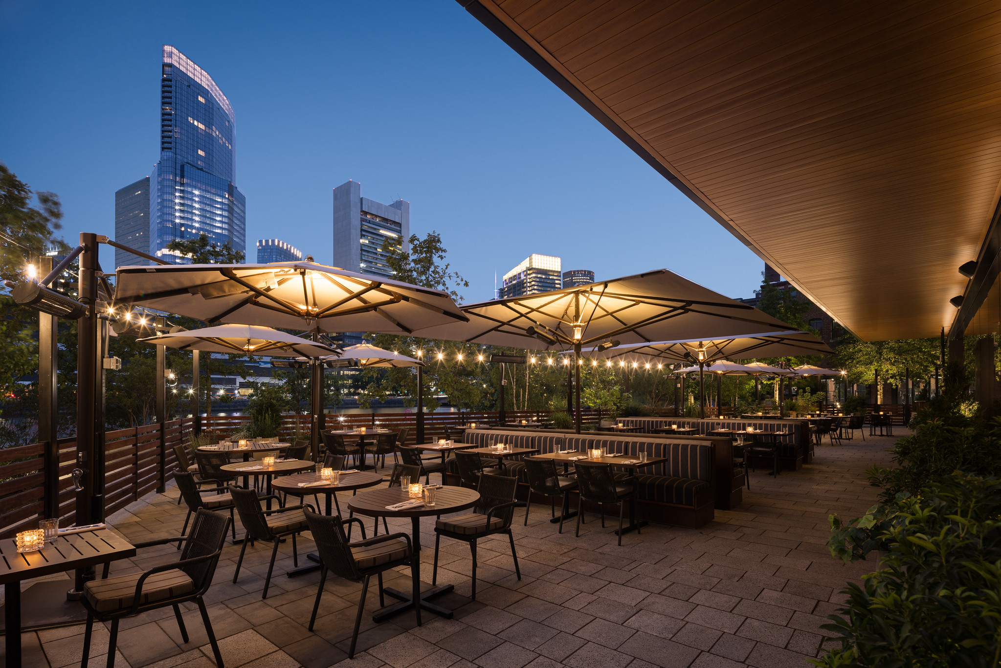 Outdoor terrace at Hawksmoor Boston at dusk, with canopied tables and chairs and the city skyline lit behind.