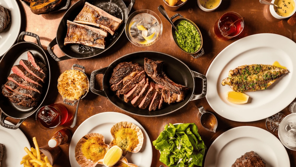 A selection of steaks, sides and starters on a table pictured from above.