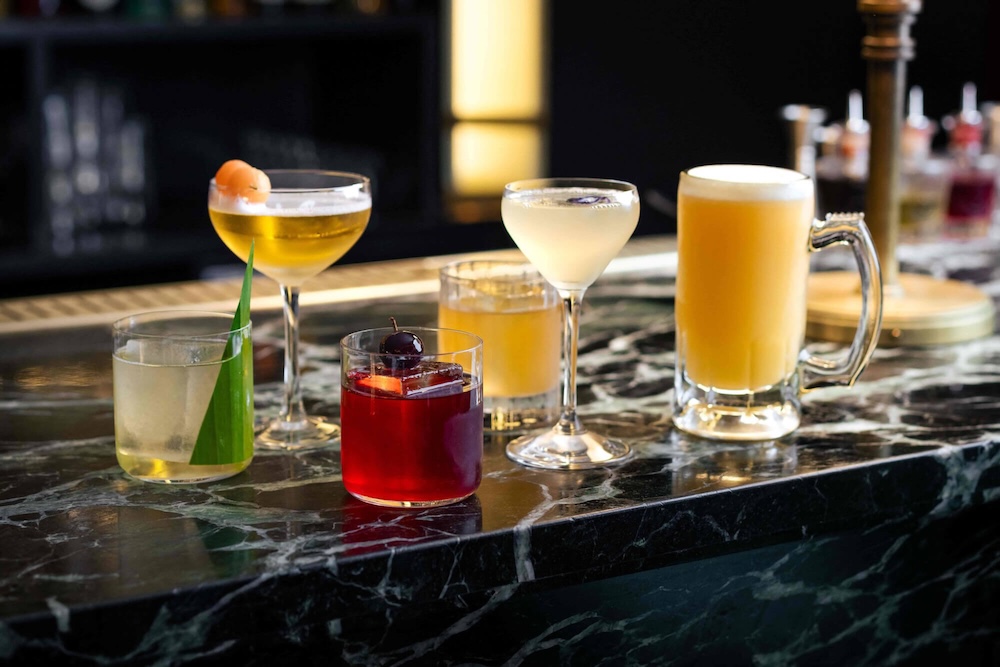 A selection of six Hawksmoor cocktails, including a Margarita and an Old Fashioned on a black marble bar.