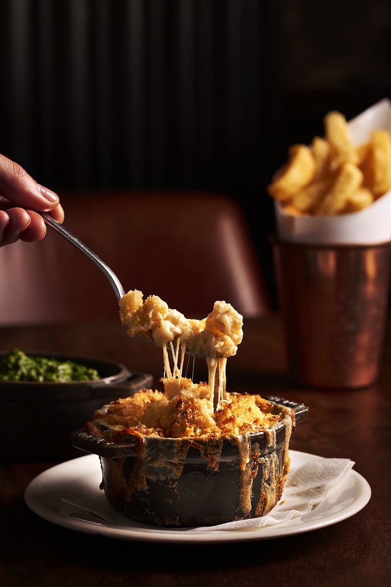 Macaroni and cheese in a cast iron dish with a cheese pull as a fork picks up some food