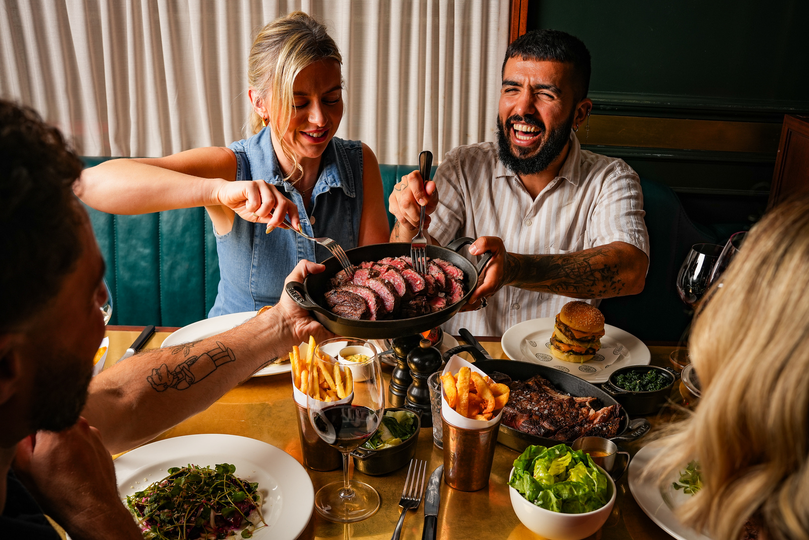 A table surrounded by patrons, a skillet of sharing steak being held up for the guests to share
