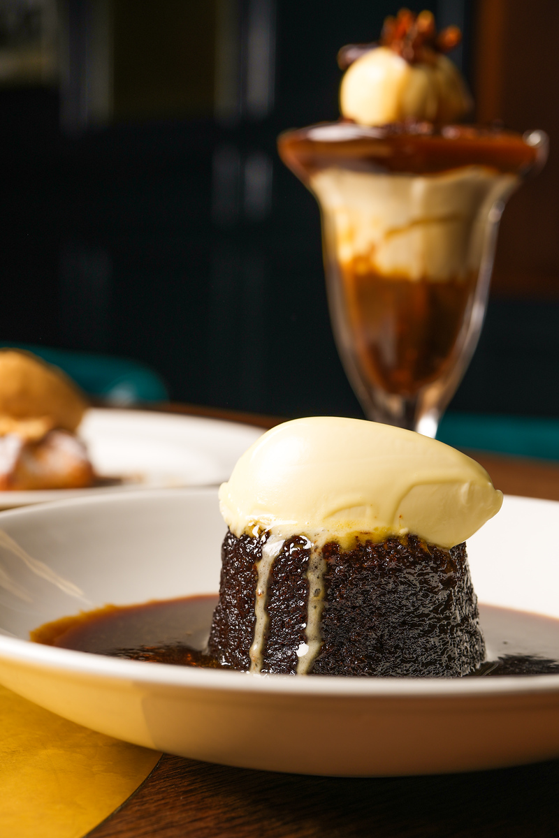 Sticky toffee pudding topped with clotted cream on a white plate