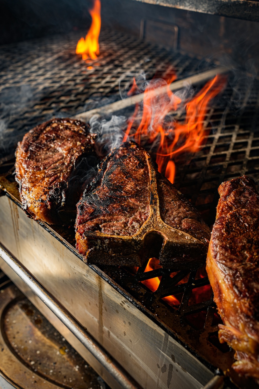 Three large cuts of steaks on the grill with open flames.