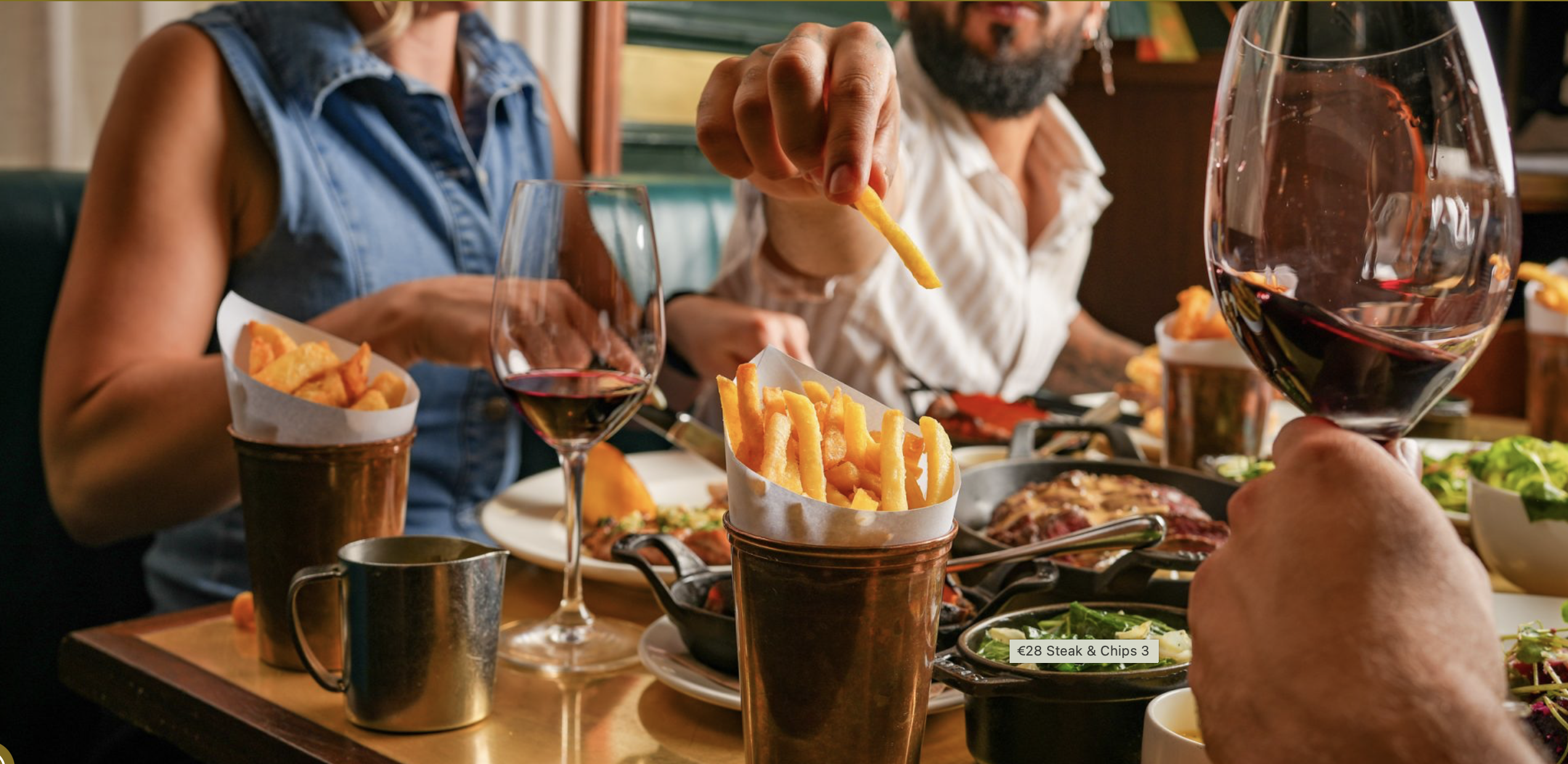People sat at a booth eating fries and drinking wine, with a table full of food