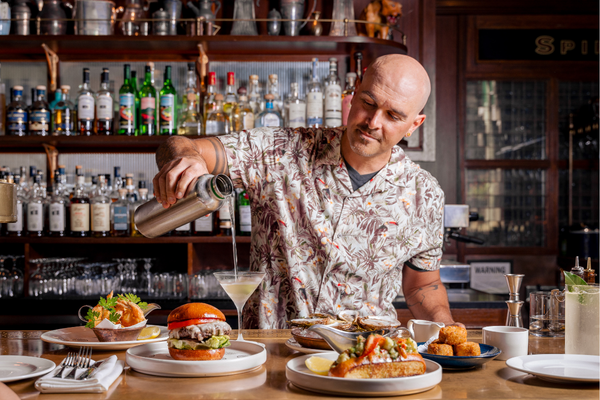 A casually dressed bartender pouring a cocktail behind the bar