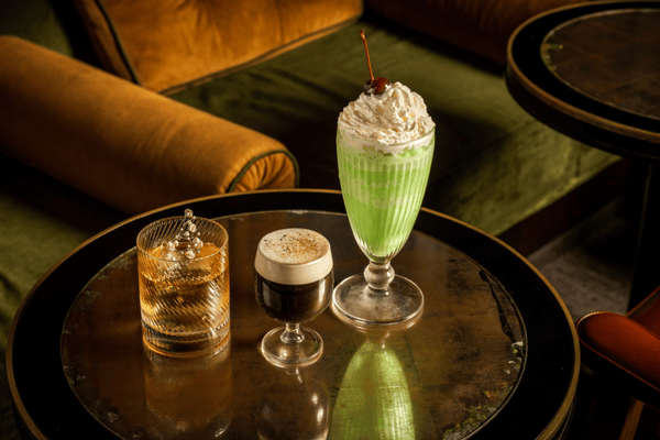 A collection of 3 St Patrick's Day themed cocktails on a small cocktails table in low lighting.