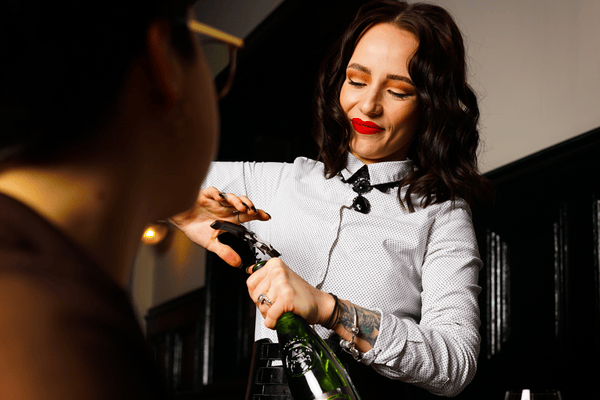 A female memeber of staff opening a bottle of champagne