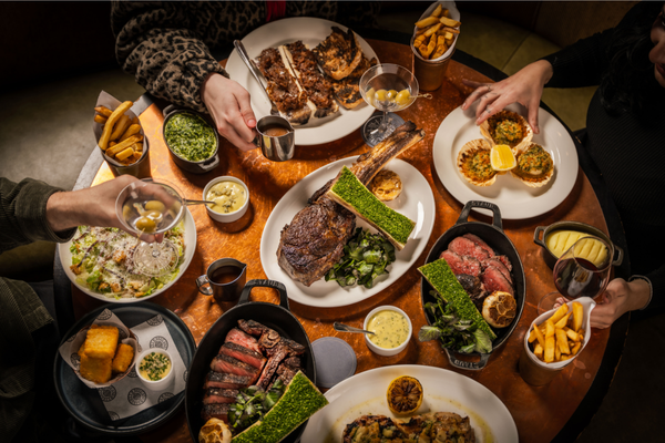 A round table shot from above laden with a selection of sharing steaks, starters and side dishes