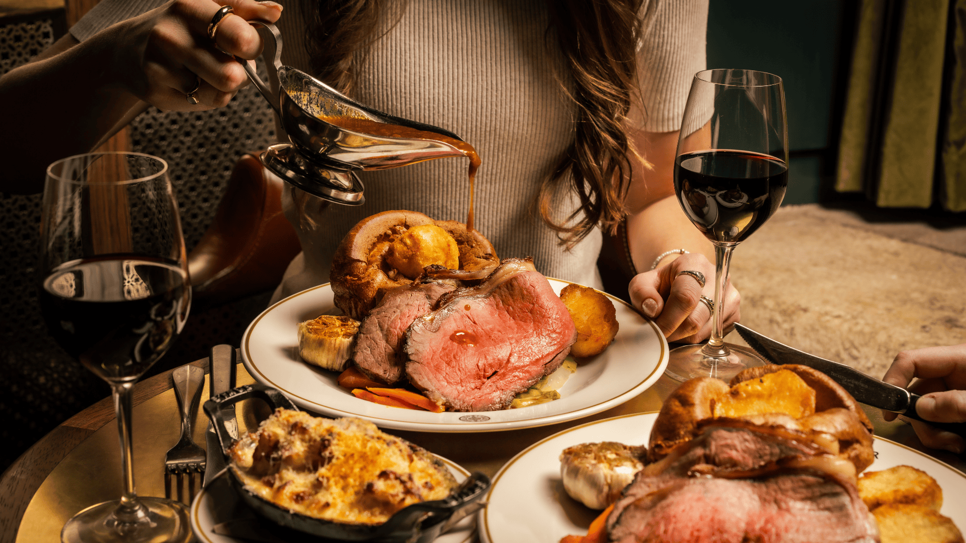 Two traditional British Sunday Roasts on a table. A female hand pouring the gravy from the jug