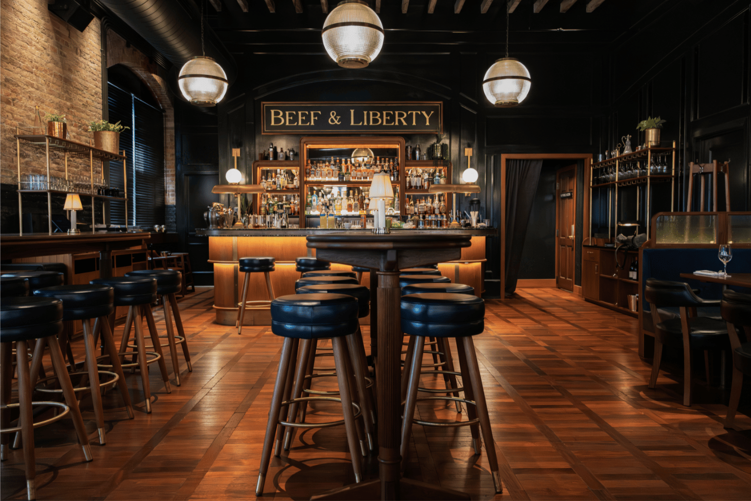 Cocktail bar interior with wood flooring, circular stools, art deco lighting, and a central marble counter set against shelves of spirits and a Beef & Liberty sign