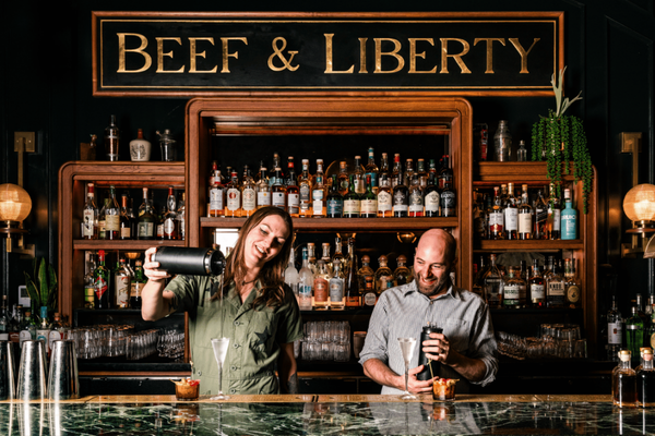 Two members of staff mixing and pouring drinks behind the bar in Beef & Liberty Room