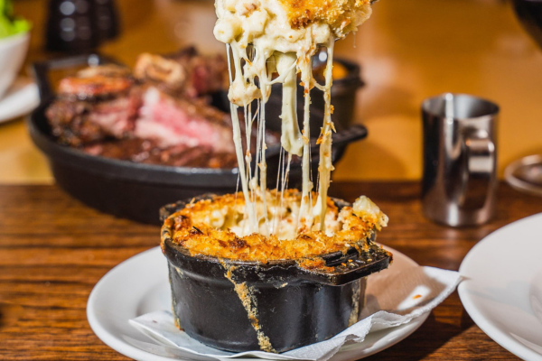 Mac and cheese in a cast iron dish, with a fork full being lifted with a generous cheese pull
