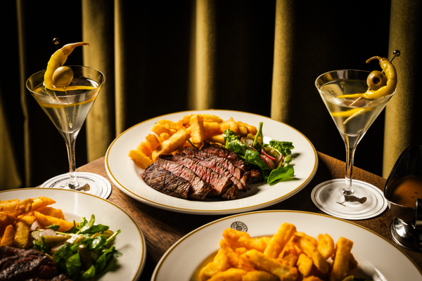 Steak and beef fat fries, on the table with martinis, against a green curtain
