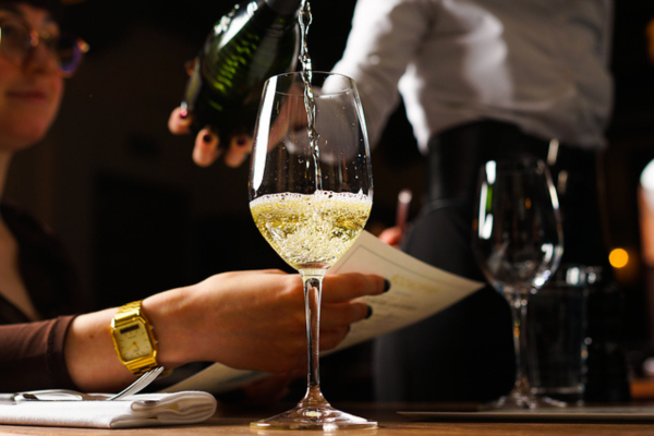 A glass of white wine being poured in the foreground, a memeber of staff in the background