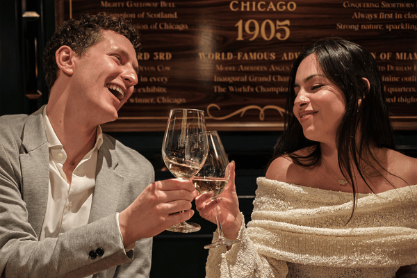 Couple on a date night at Hawksmoor, laughing and clinking glasses of white wine against a gold-lettered wall