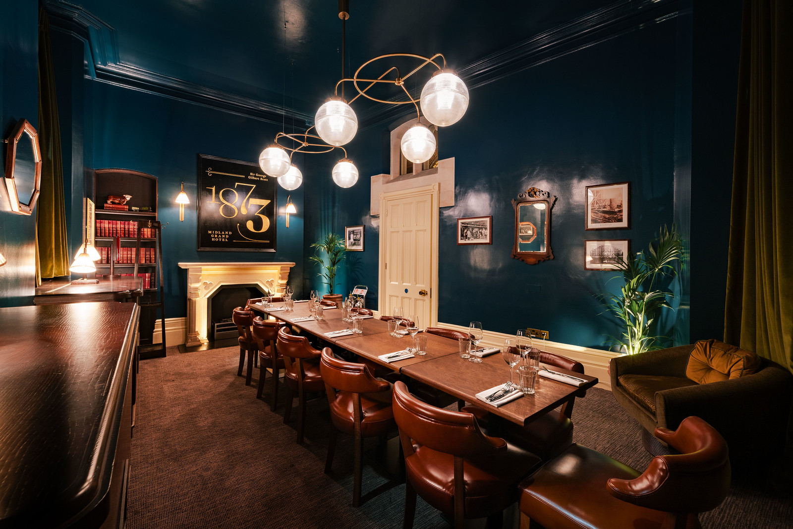 A wide shot of a private dining room with high ceilings, painted dark blue, with a handsome wooden table for 12 guests in the middle of the room