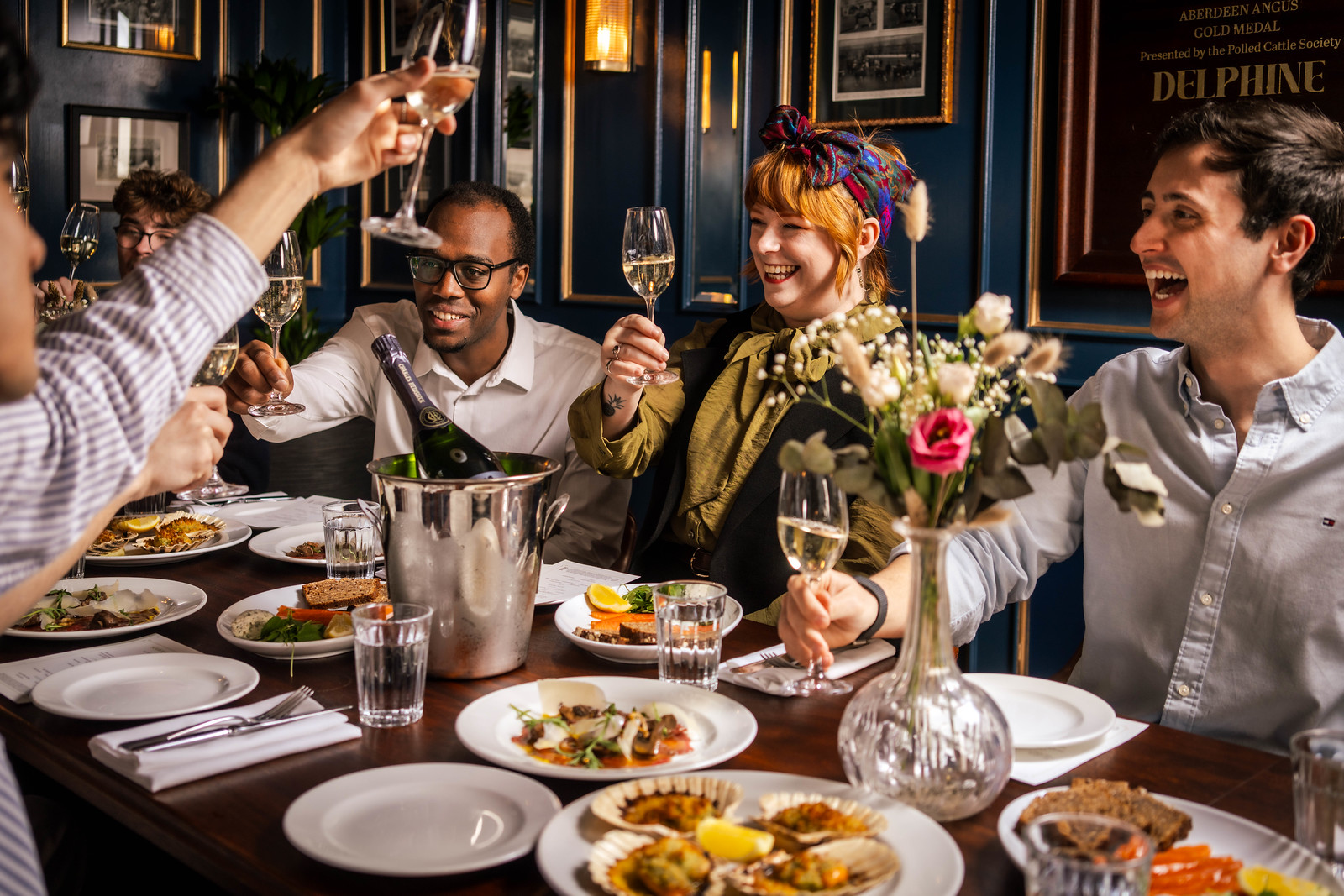 A large group of friends celebratins and raising galsses around a large table in a private dining room