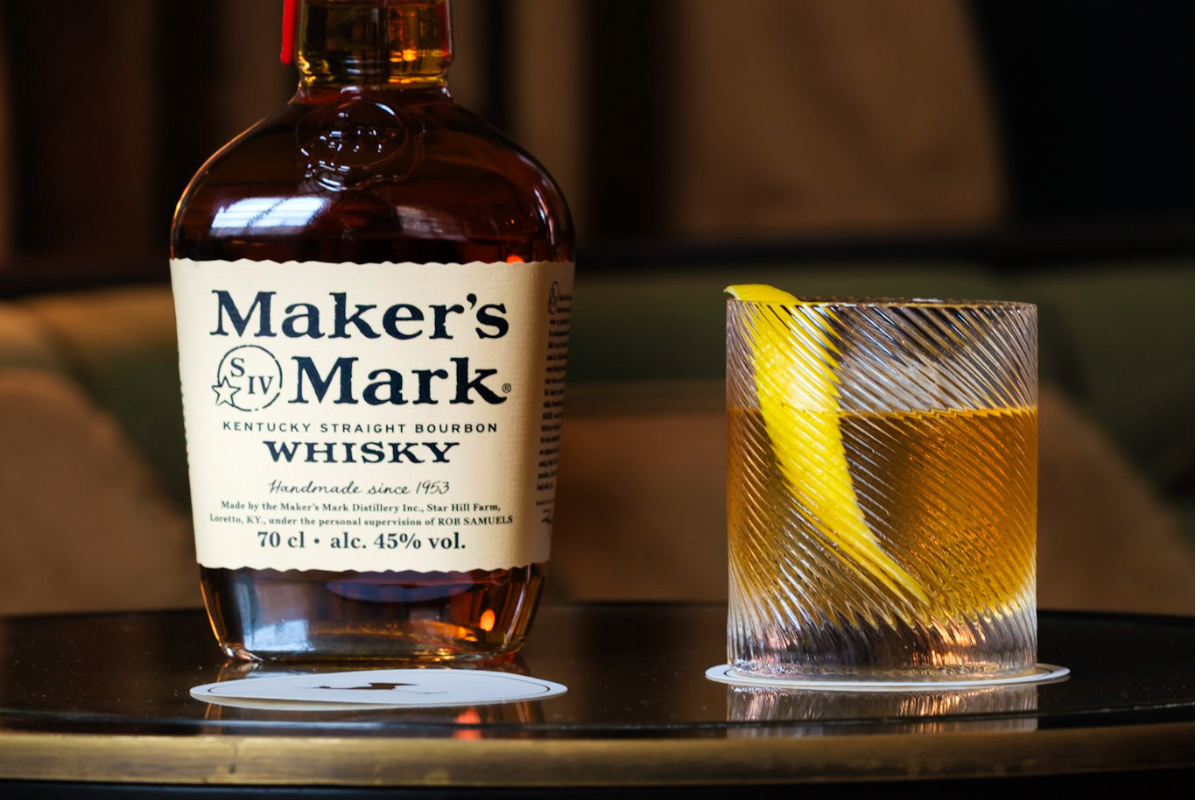 A bottle of Maker's Mark next to a cocktail with a lemon twist garnish