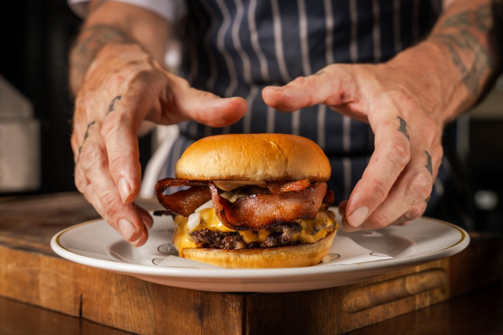 Calfreezy x Hawksmoor 1 Chef hands about to lift up the Burgurr off the plate