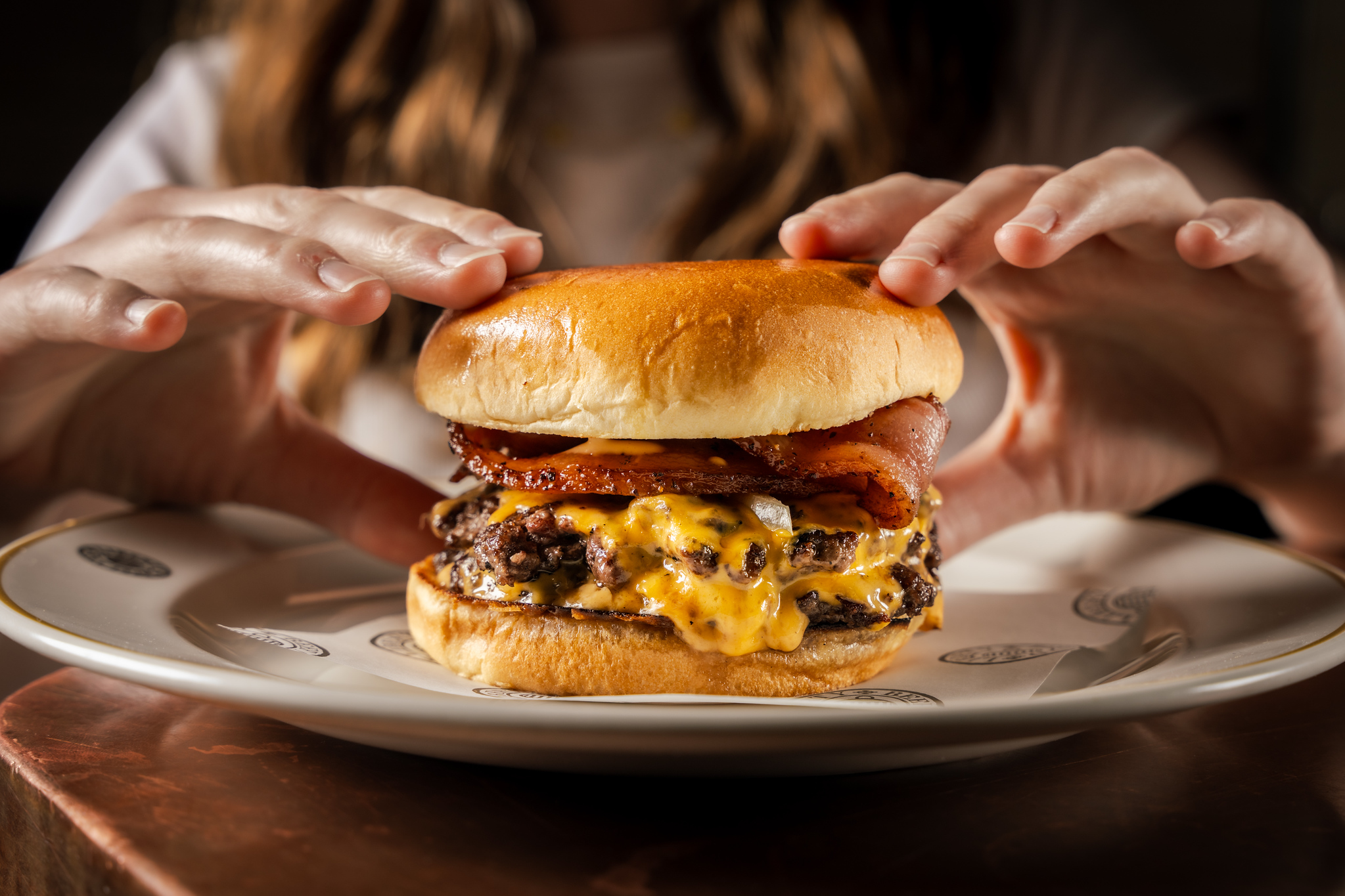 Close-up shot of the Burgurr on a white plate, with two hands preparing to pick it up