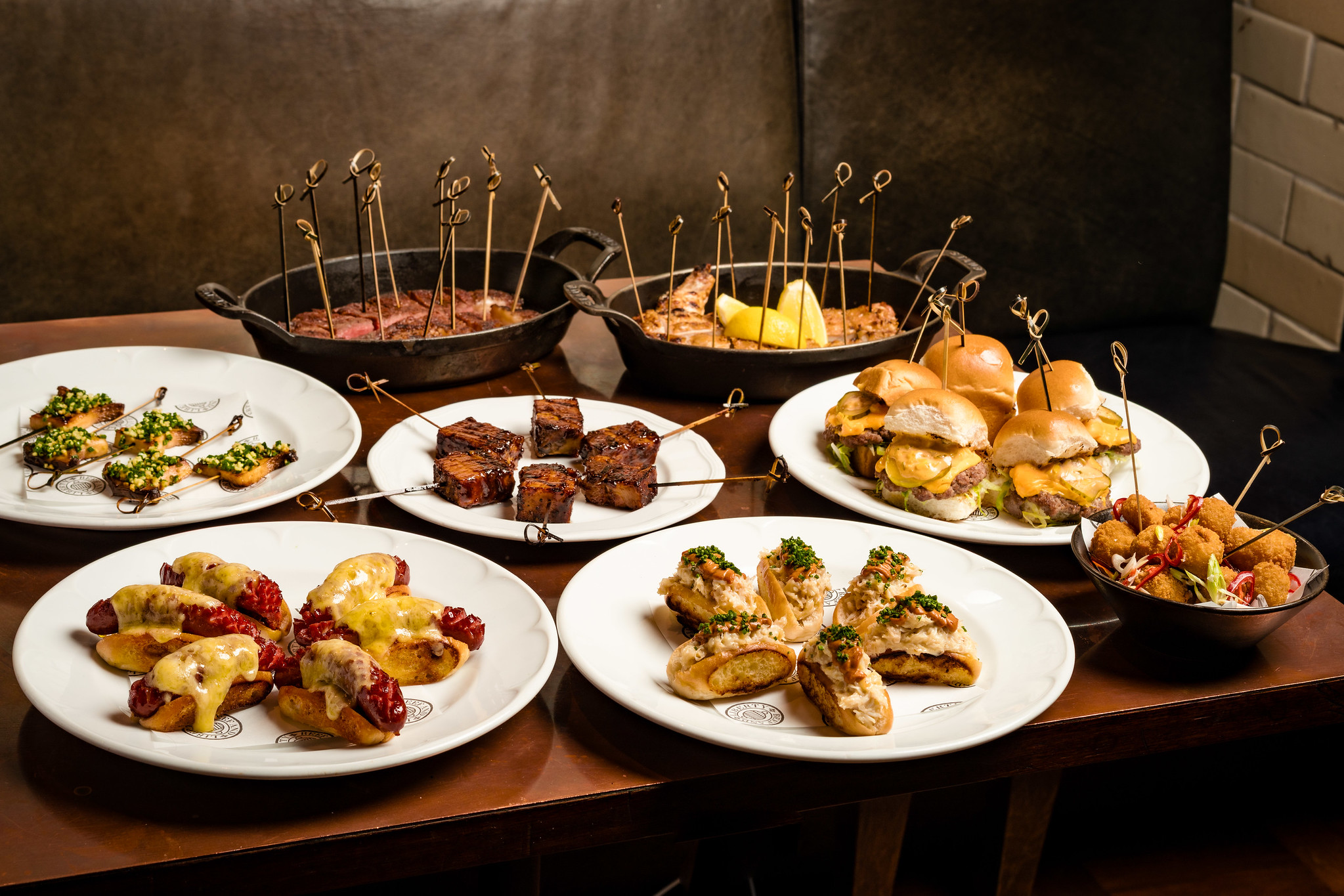 Selection of Hawksmoor canapés and bowl food laid out on a wooden table, including sliders, skewers and small plates