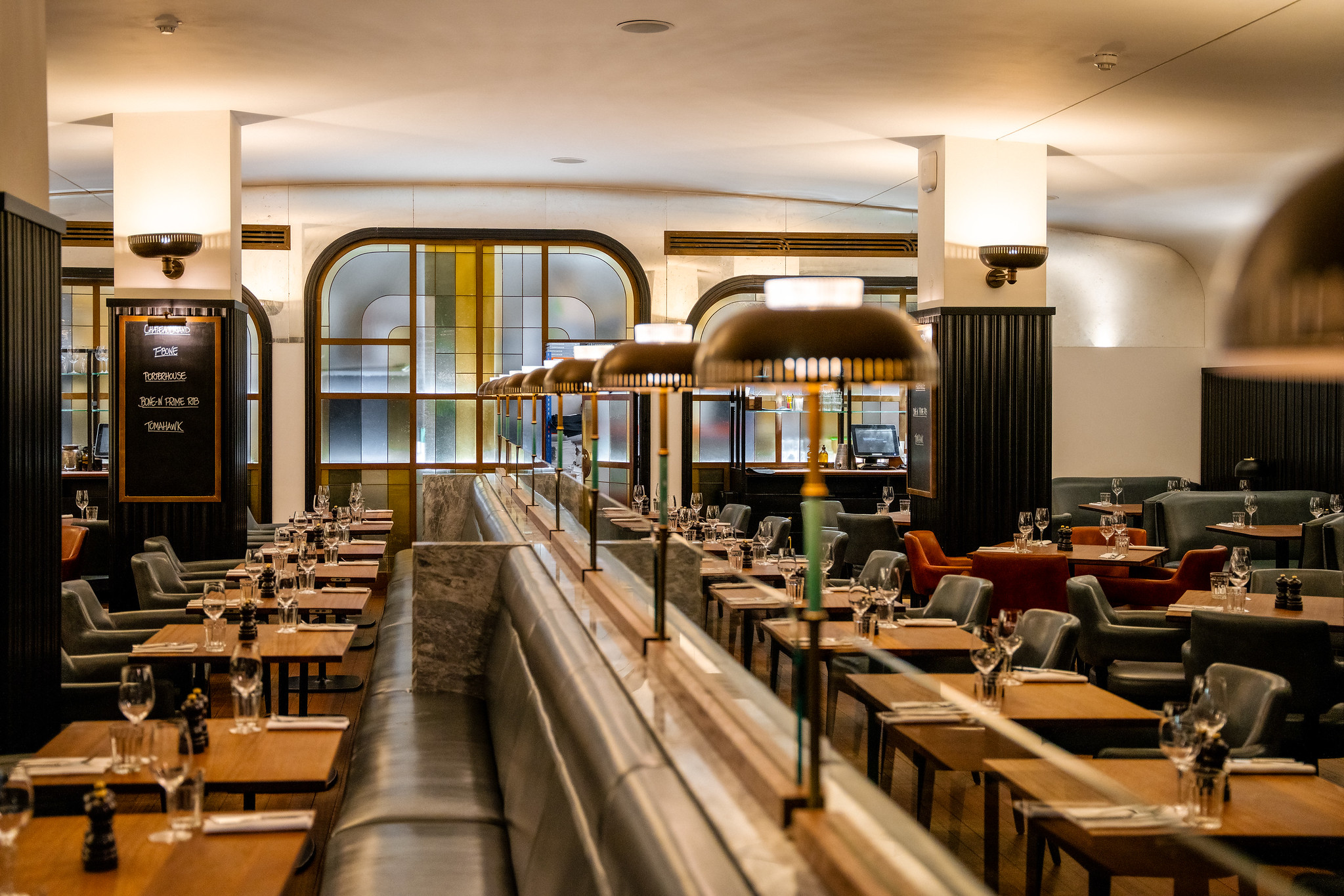 The dining room at Hawksmoor Knightsbridge, with tables either side of a central banquette under brass pendant lamps.