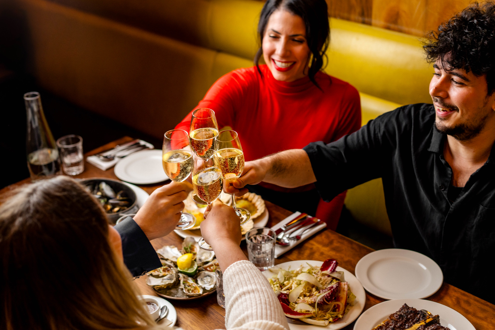 Four friends raising glasses of white wine over a table of oysters, salad and steak at Hawksmoor