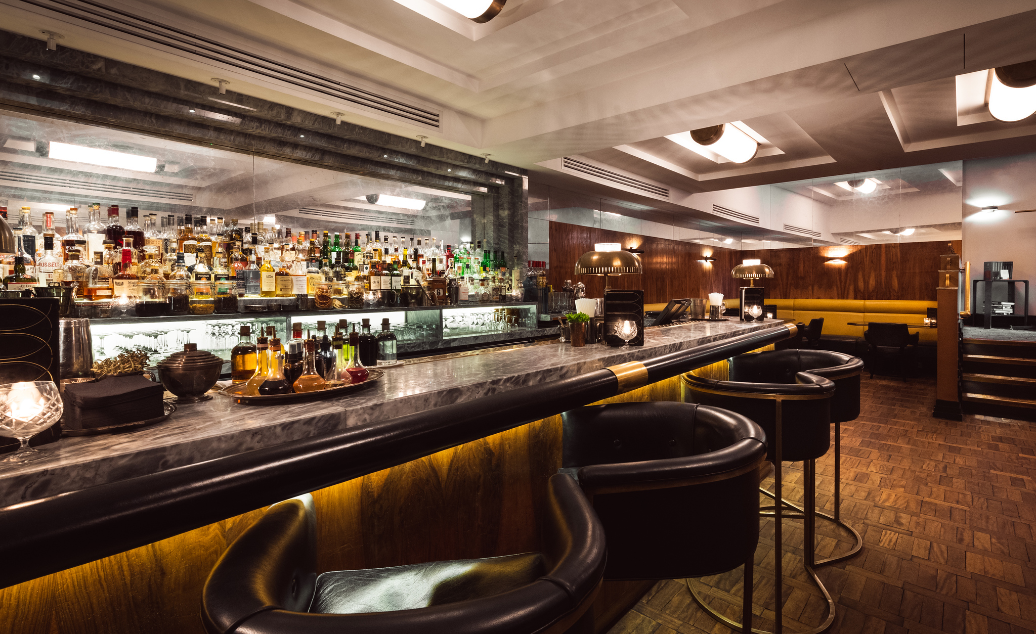 The bar at Hawksmoor Knightsbridge, with leather stools along a marble-topped counter and backlit bottle shelves.