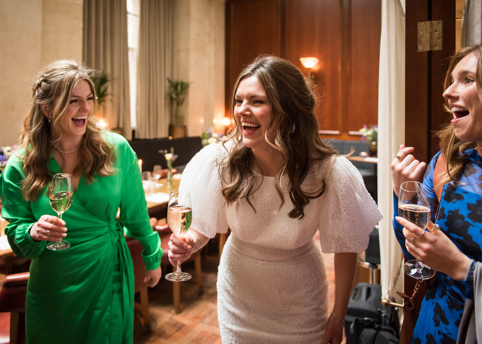 Three friends laughing together with glasses of champagne at a private wedding celebration at Hawksmoor