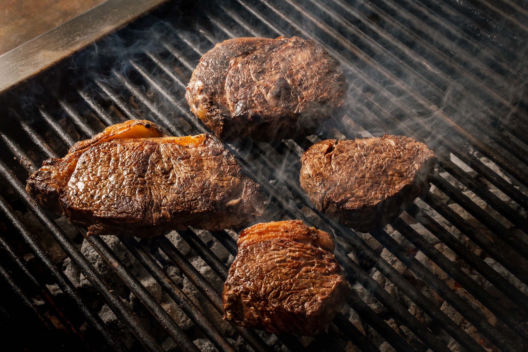 Four steaks cooking over the charcoal grill at Hawksmoor, crusted and smoking on the bars