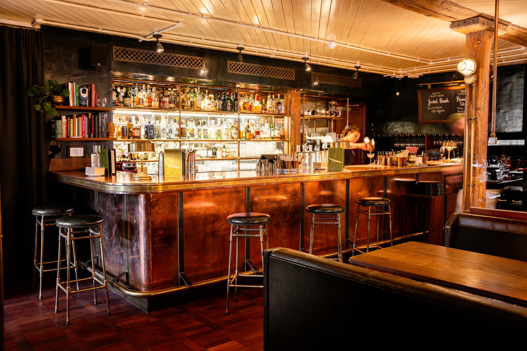 The bar at Hawksmoor Borough, copper-fronted with a brass foot rail, bar stools, a bottle-lined back bar and leather banquettes alongside