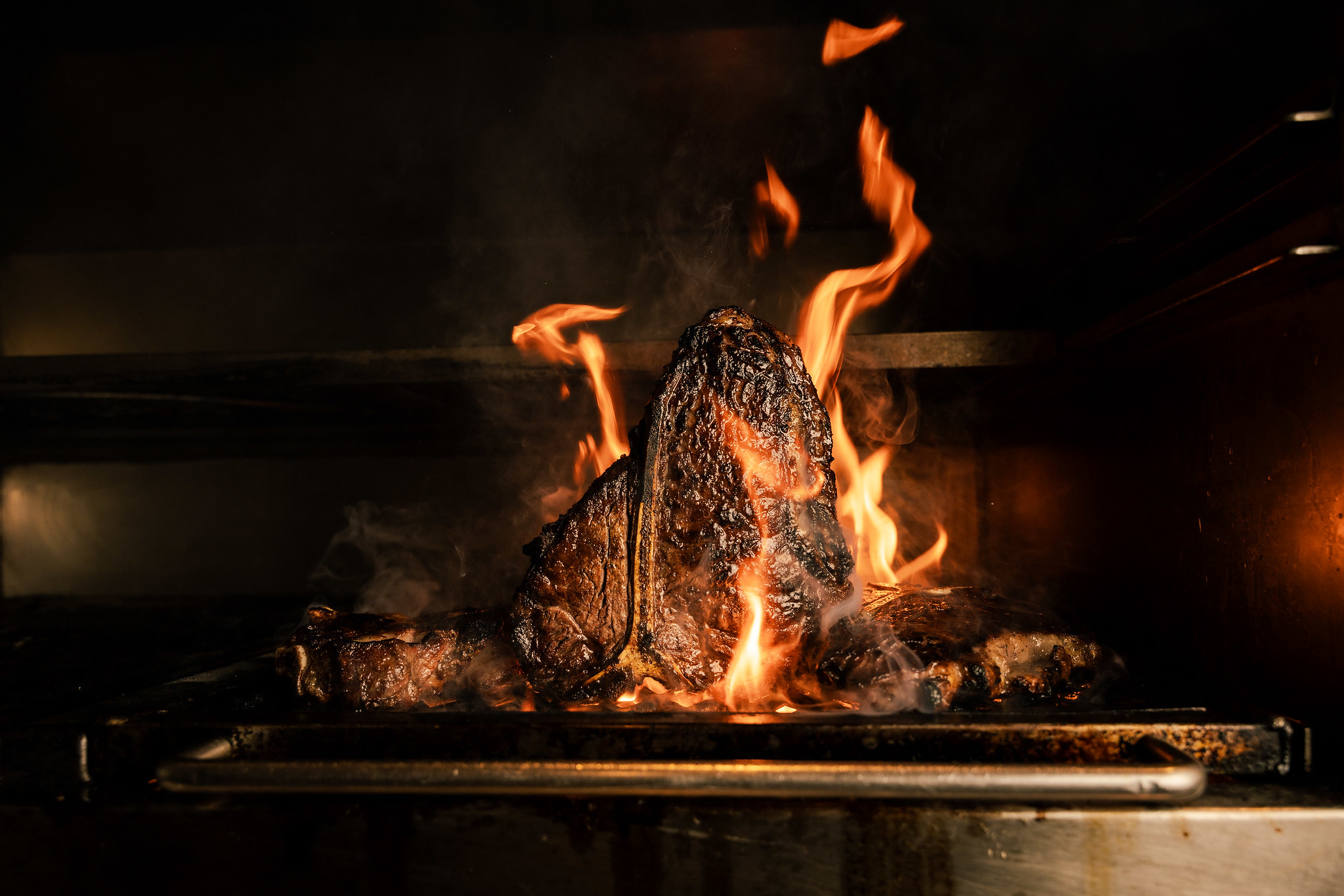 Porterhouse steak searing over open flames on a charcoal grill at Hawksmoor